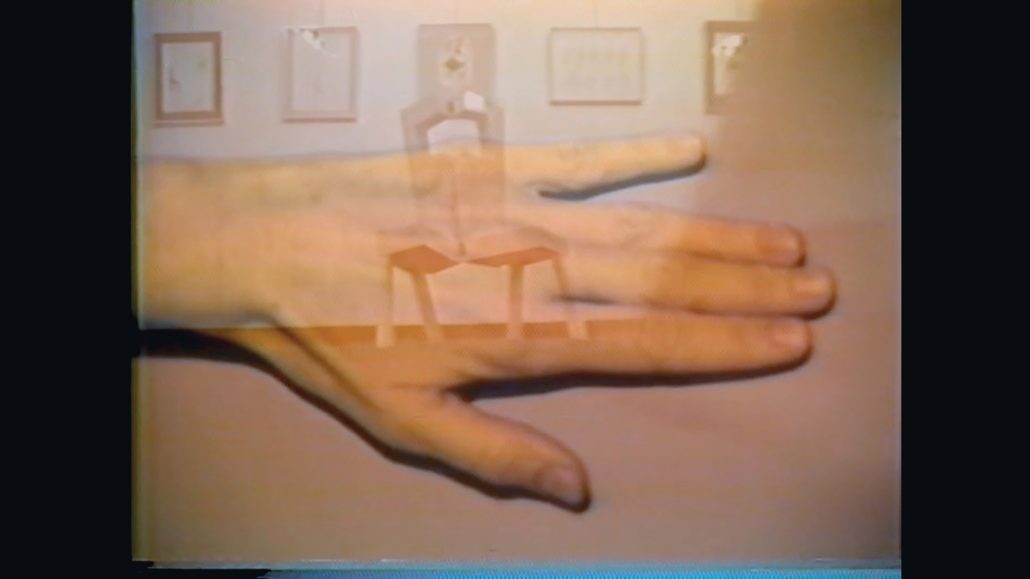 Primer plano de una mano izquierda con los dedos separados sobre un fondo beige. La mano se superpone a una imagen tenue de una silla y de cuadros enmarcados en una pared, creando un efecto de doble exposición.